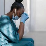 Hospital Inferno Kills 14 Newborns Healthcare worker in scrubs sitting against a wall with head bowed