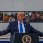 Trade War Escalates With Name Bomb Donald Trump speaks at a podium with arms outstretched