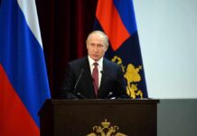 Seven Insiders Emerge In Putin Succession speaker at podium with flags in background