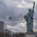 Met Retreats After Antisemitism Uproar Statue of Liberty replica with cloudy sky and city buildings