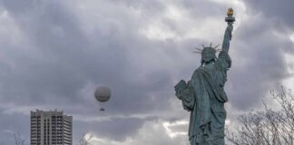 Statue of Liberty replica with cloudy sky and city buildings