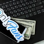 Teacher Booted Over OnlyFans Smartphone with OnlyFans sticker and cash on a laptop keyboard
