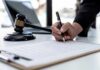 Sky-High Gun Fees On The Chopping Block Hand signing legal document beside gavel and laptop