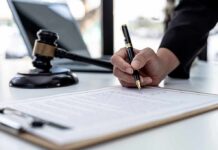 Sky-High Gun Fees On The Chopping Block Hand signing legal document beside gavel and laptop