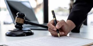 Sky-High Gun Fees On The Chopping Block Hand signing legal document beside gavel and laptop