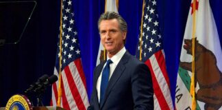 Union Fury Erupts Over Hollywood Deal Man in suit speaking at a podium with American and California flags