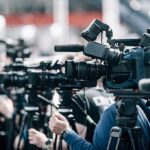 Water Systems Breached — Iran Link Eyed Broadcast cameras on tripods at a press event