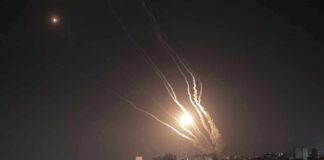 Night sky above a city with multiple rockets arcing and bright explosions