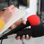 Man Survives Two Hours Inside Garbage Truck Journalist holding two microphones while writing in a notebook