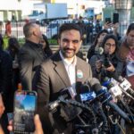Smiling man at outdoor press conference with microphones