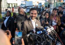 Smiling man at outdoor press conference with microphones
