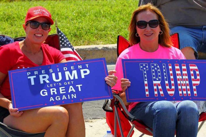 Two women seated outdoors holding blue pro-Trump signs
