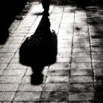Masked Ambush In Central Park Silhouette shadow of a person walking on a wet pavement
