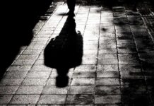 Masked Ambush In Central Park Silhouette shadow of a person walking on a wet pavement