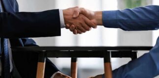 Two people shake hands while exchanging cash under a table