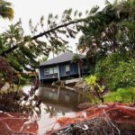 Midnight Roar Triggers Mass Evacuation house by flooded canal with fallen palm trees