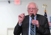 Bernie Sanders Invades Trump Country – What States? Bernie Sanders speaking into a microphone at an indoor event