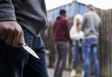 Person holding a folding knife near a group of people in an alley