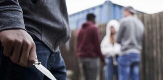 Person holding a folding knife near a group of people in an alley