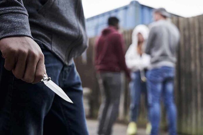 Person holding a folding knife near a group of people in an alley