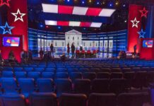 No Debates Anymore And Here’s Why Debate stage with red and blue lighting and empty audience seats