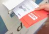 Election Safeguards Put To The Test Hand dropping mail-in ballots into a drop box