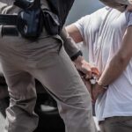 Arrest After Shocking Classroom Clash police officer handcuffing a person beside a vehicle