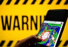 Hand holds smartphone showing cyclone radar map against warning sign