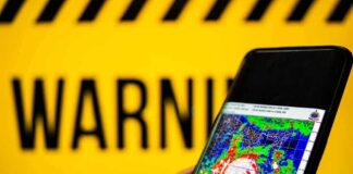 Hand holds smartphone showing cyclone radar map against warning sign