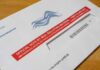 Mail-in ballot envelope with red label on wooden table