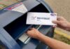 Person mailing a ballot into a blue street mailbox