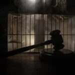 Judge’s gavel in silhouette before prison bars