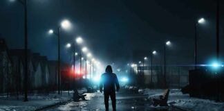 Silhouetted person walking on a wet, snowy street at night