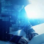 School Data RAIDED – Millions At Risk Hooded figure using a laptop with digital code overlay