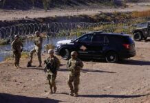 Soldiers stand near barbed wire beside a police SUV