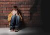 boy sitting against brick wall covering his face