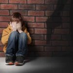 boy sitting against brick wall covering his face