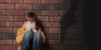 boy sitting against brick wall covering his face