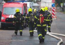 Deadly Blaze, Gunman Triggers Citywide Shock Firefighters walking toward a scene with hoses and a red emergency van