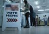 Senator Seeks Answers On Military Election Role Vote here sign at a polling station with people in line