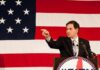 State Department Hits Hong Kong Hard Speaker in suit pointing during speech before large American flag