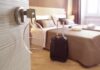 Hotel room key in door with suitcase by bed