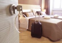 Hotel room key in door with suitcase by bed