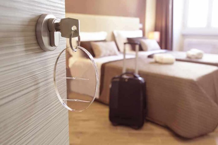 shutterstock_388726060 Hotel room key in door with suitcase by bed